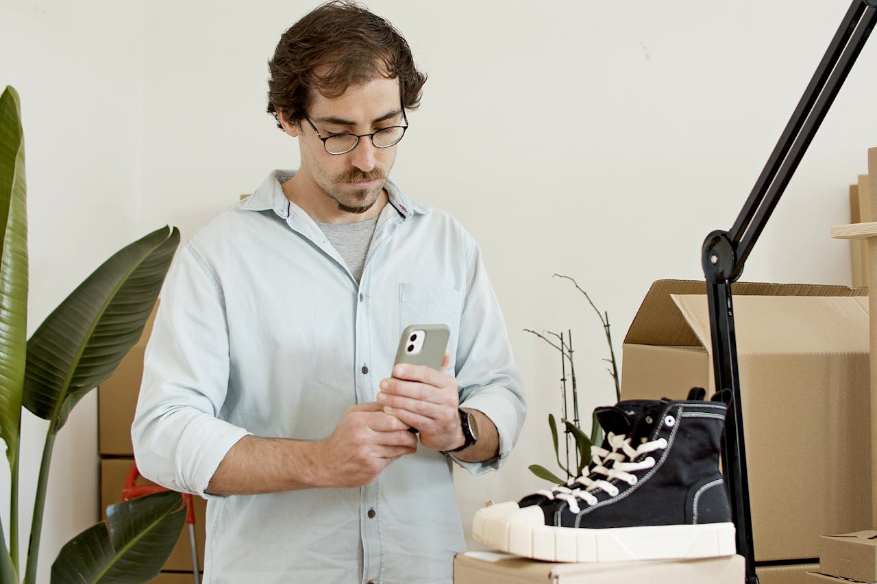 Man uses phone to photograph sneakers in an indoor business setup with boxes.
